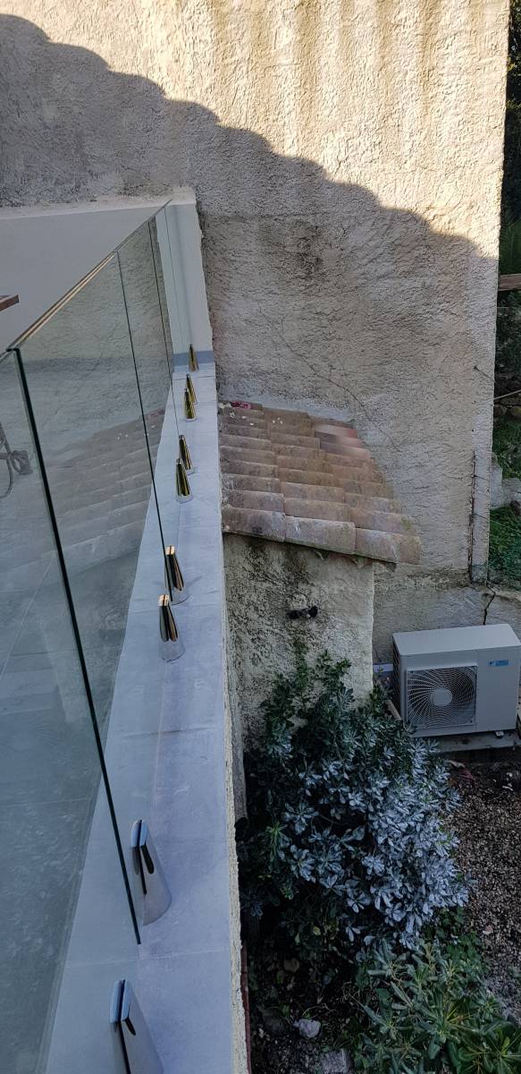 Installation de garde-corps en verre clair trempé avec fixation par pinces en inox, mettant en avant un style contemporain.
