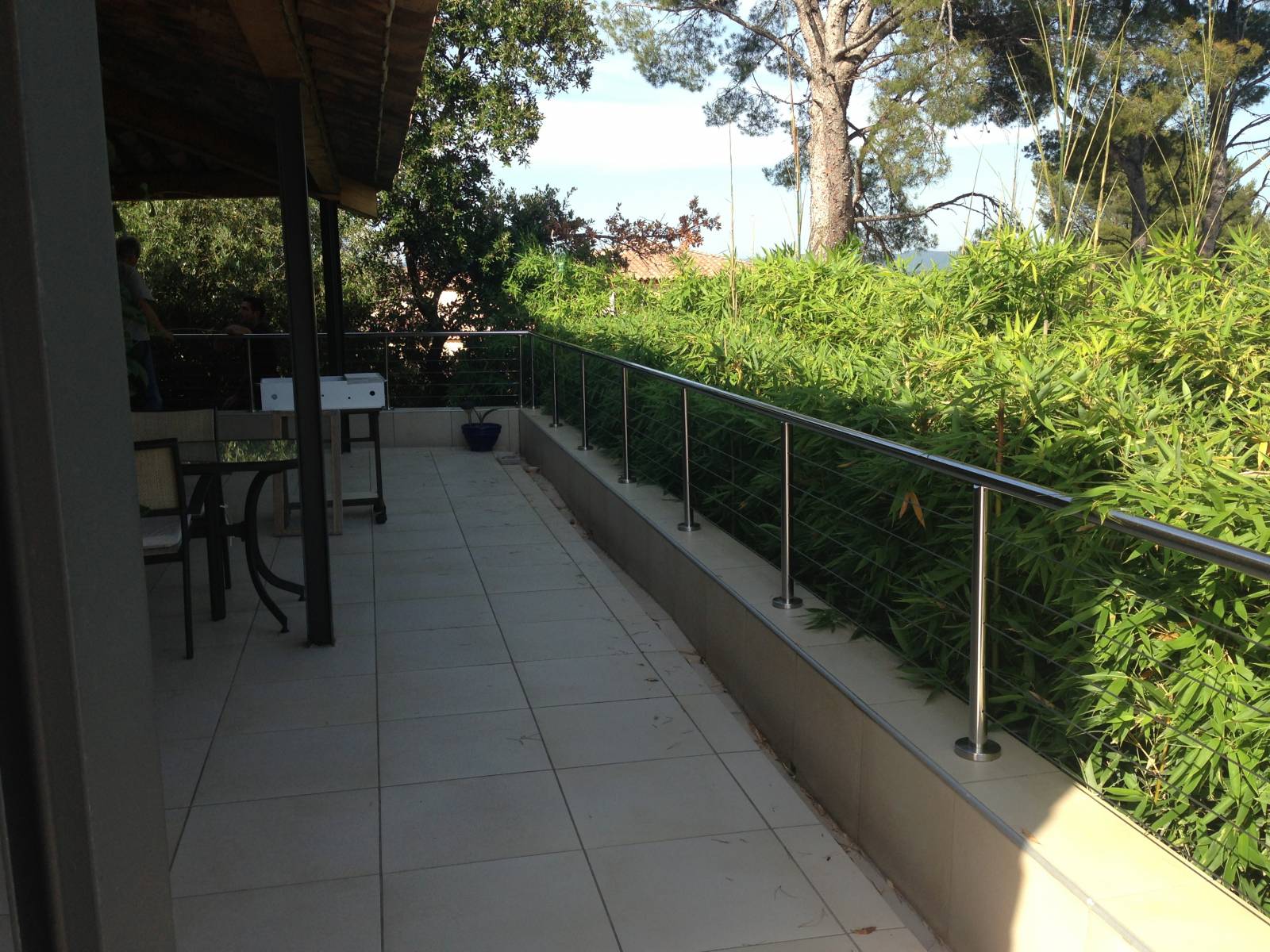 Garde-corps en inox poli avec câbles, installé sur une terrasse, offrant une vue dégagée sur un jardin verdoyant.