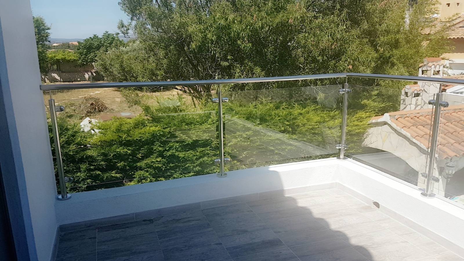 Vue rapprochée d'un garde-corps en inox poli miroir et verre feuilleté, installé sur un acrotère pour sécuriser la terrasse.