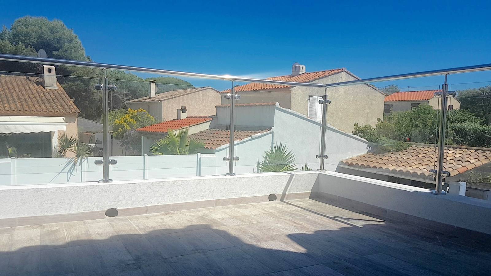 Détail des pinces en inox massif fixant un panneau de verre clair, offrant sécurité et transparence sur une terrasse.