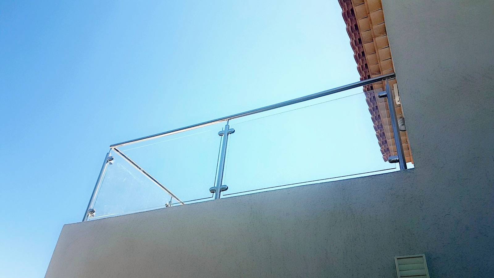 Détail des pinces en inox massif fixant un panneau de verre clair, offrant sécurité et transparence sur une terrasse.