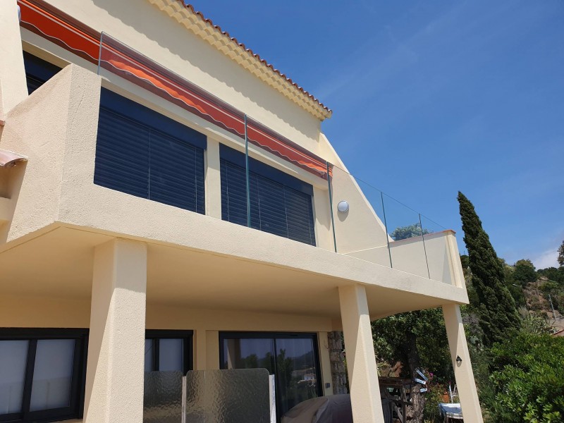 Façade d'une maison surplombant la mer, avec un garde-corps en verre pour une vue dégagée.