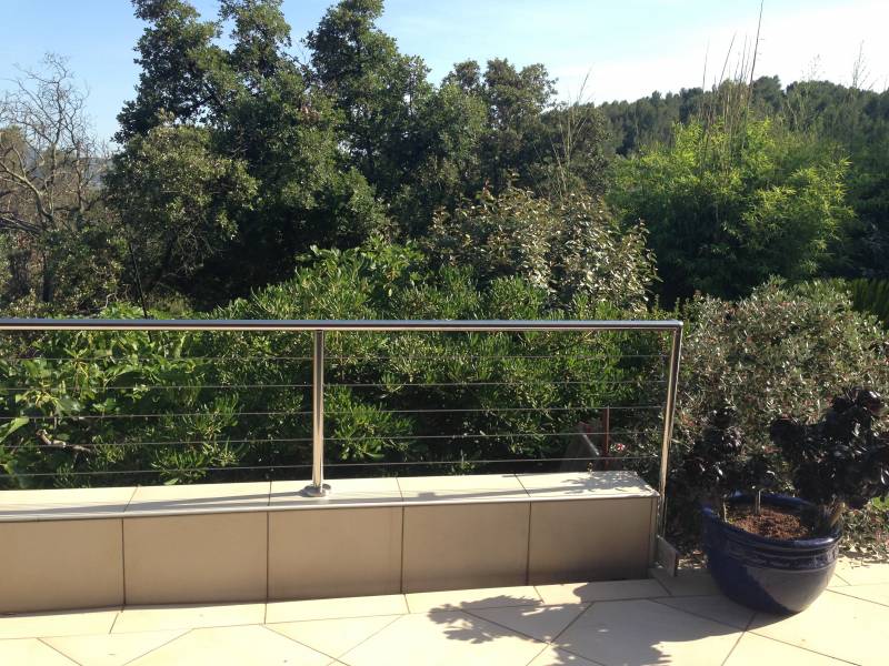 Garde-corps en inox poli avec câbles, installé sur une terrasse, offrant une vue dégagée sur un jardin verdoyant.