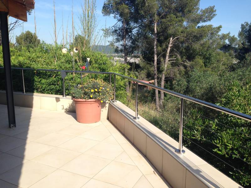 Garde-corps inox avec tubes ronds et câbles, installé sur une terrasse surélevée, se mariant parfaitement avec la nature environnante.