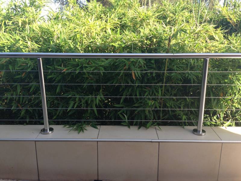 Garde-corps en inox poli entourant une piscine, avec des plantes luxuriantes en arrière-plan, garantissant sécurité et esthétisme.