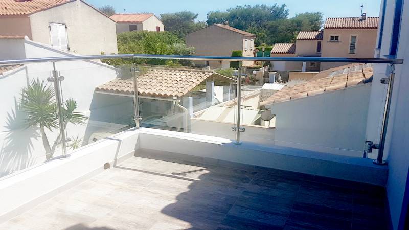 Garde-corps en inox poli miroir avec remplissage en verre feuilleté clair, installé sur une terrasse avec vue sur le jardin.