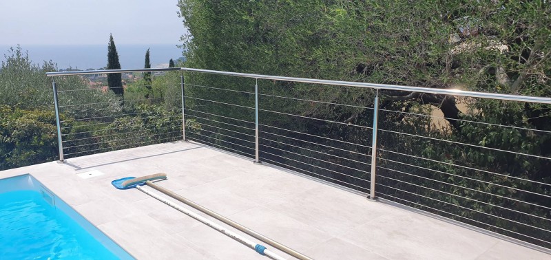 Garde-corps en inox poli miroir avec remplissage en câbles inox, installé sur une terrasse rénovée en bord de mer.